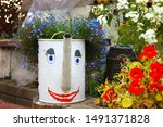 Small photo of A watering can painted in cloy stands on a bench in the garden.