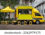 Small photo of A small yellow truck converted into a mobile coffee shop with yellow seats and tents serving customers.