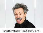 Small photo of Portrait of jocular aging man with grey long hair sticking his tongue out in Einstein manner.