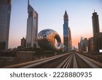 Small photo of Dubai, UAE - 10th october, 2022: metro train on railway in Dubai with museum of future and sunset sky background
