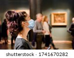 Protection from the virus. A tourist visits the sights of the Museum in a medical mask. People and pictures in the background. The concept of a viral pandemic and maintaining distance
