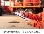 Small photo of Action of safety officer is check on checklist document during safety audit and risk verification at drilling site operation with blurred background of mount truck rig. Selective focus at hand.