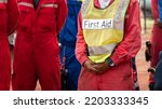 Small photo of Group meeting of field operation staffs with a man who wear "First Aid" vest, preparing for emergency drill and practice scenario at construction site. Industrial people working scene photo.