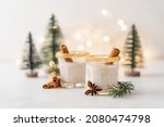 Small photo of Eggnog with cinnamon and nutmeg for winter holidays. Christmas traditional eggnog in glasses on white background with garland and small trees