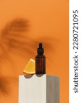 Small photo of Dark glass cosmetic bottle and orange slice on wooden podium and orange background. Vitamin C beauty product concept