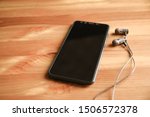 Dark headphones and smartphone lies on wooden background. Design layout, smart phone with black screen and wired headphones with copy space on the office desk. Top view.