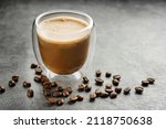 latte in a double-walled glass cup close-up. A glass of coffee and coffee beans on a dark surface.