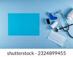 Medical mask, stethoscope, oximeter, bottle of pills and inhalers on light blue background with vibrant blue rectangular sheet of paper for text placement. Asthmatic breathing symptoms Concept
