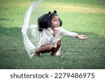 Happy smiling African girl with black curly hair with umbrella under raindrops fall while playing outdoor green park, beautiful kid playing outside garden on rainy day, cute child playing in the rain