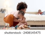 Small photo of Happy African family spending time together, brother boy with black curly hair try to hold and lift up little cute toddle baby infant kid on floor with blurred background of dad reading book on bed.