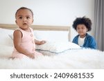 Small photo of Happy African siblings in family, portrait of cute toddle baby infant sister girl sitting on white bed with her brother boy with curly hair as blurred background. kid spending time together.