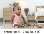 Small photo of Portrait of smiling African cute toddle baby infant kid playing toys while sitting on floor in bedroom at home. Child and happy childhood