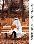 Small photo of Person in a ghost costumes for Halloween party. in autumn park Halloween ghost with halloween pumpkin Jack-o-lantern.