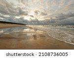 Small photo of Wide view over a deserted stretch of beach, in the foreground shallow water with view leading to the horizon, above partly dramatic clouds announcing a change of weather, Slowinski Park Narodowy