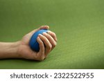 Hands of a man squeezing a blue stress ball on the yoga mat