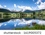 beautiful reflection of the rocky mountains in the sprague lake with green pine forest in the background in summer with blue sky in the rocky mountain national park, colorado, united states of america