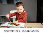 A cute happy little toddler boy of two years old draws with markers in the album in the children's room at home. Educational activities for kids. Selective focus