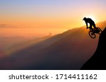 Silhouette of a mountain biker enjoying downhill during the sunset. Cyclist silhouette on the hill beautiful colorful sky and clouds in the background.