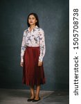 Small photo of Studio portrait of a stylish, attractive, confident and elegant Indian Asian woman in a floral blouse and red dress. She looks somber and neutral as she stands for her profile head shot.