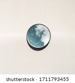 Elegant and artistic image of a mini circular mirror with reflections of the blue sky with clouds on a light and bright brown background