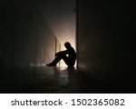 Silhouette of depressed man sitting on walkway of residence building. Sad man, Cry, drama, lonely and unhappy concept.