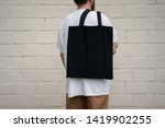 Urban mockup of tote bag. Men holding black cotton tote bag on a brick wall background. Template can be used for you design 
