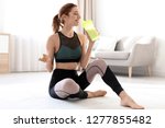 Young sporty woman with bottle of protein shake sitting on floor at home