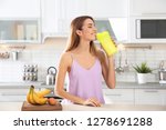 Young woman drinking protein shake near table with ingredients in kitchen