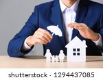 Male insurance agent covering paper family and home with umbrella cutout at table, closeup