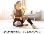Young woman with bottle of refreshing drink after fitness exercises sitting on floor at home 