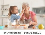 Cute girl and her grandmother cooking in kitchen