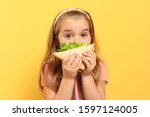 Cute little girl eating tasty sandwich on yellow background
