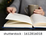 Woman with cup of beverage reading book at table, closeup