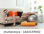 Lazy young man with sport equipment on sofa at home