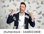 Happy young man with dollars under money rain on light background