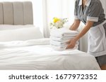 Young chambermaid putting stack of fresh towels in bedroom, closeup. Space for text