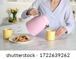 Woman pouring hot water from modern electric kettle in cup indoors, closeup