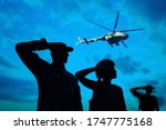 Silhouettes of soldiers in uniform saluting and military helicopter outdoors