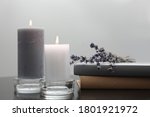Wax candles in glass holders near books and lavender flowers on table against light background