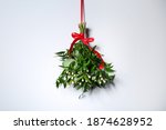 Mistletoe bunch with red bow hanging on light wall. Traditional Christmas decor