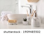 Small photo of Holder with toothbrushes, plant and different toiletries near vessel sink in bathroom