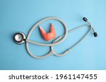 Small photo of Plastic model of afflicted thyroid and stethoscope on light blue background, flat lay