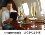 Businessman working at table in airplane during flight, focus on glass of champagne