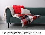 Sofa with soft pillows and warm plaids near light wall indoors