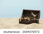 Open wooden chest with treasures on sandy beach, space for text