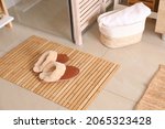 Small photo of Wooden mat and slippers on tiled floor in bathroom. Stylish accessory