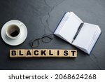 Small photo of Wooden cubes with word Blacklist, cup of coffee and office stationery on slate table, flat lay