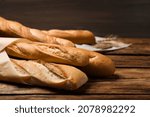 Fresh tasty baguettes and spikelets on wooden table, closeup
