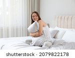 Young woman hugging pillow on comfortable bed with silky linens