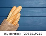 Tasty baguettes in package on blue wooden table, top view. Space for text